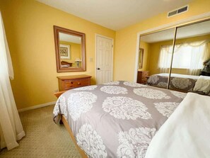 A bedroom with a bed, a dresser, a mirror, and a door. - Las Palmas Resort #107 | All-Inclusive Amenities (Saint George)