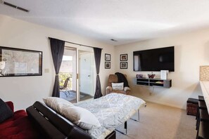 A bedroom with a bed, a chair, a TV, and a sliding door to a balcony.