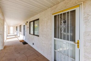 A corridor with a tiled floor, a door with a glass panel and a decorative handle, and a window with a metal grille.