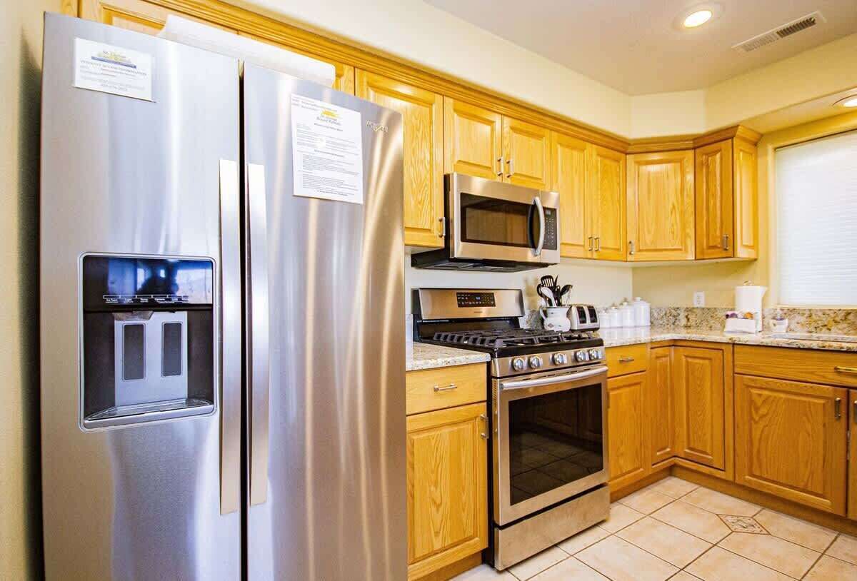 A kitchen with stainless steel appliances, wooden cabinets, and a tiled floor.