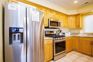 A kitchen with stainless steel appliances, wooden cabinets, and a tiled floor.