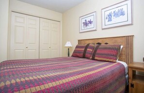 Un dormitorio con cama, mesita de noche, lámpara y dos cuadros en la pared.