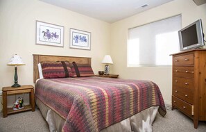 A bedroom with a bed, a wooden dresser, a television on top, and two wall-mounted pictures.