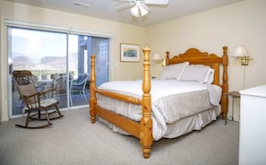 Quarto com cama de dossel, uma cadeira de balanço, mesa de cabeceira com abajur e vista através de uma porta de vidro deslizante.