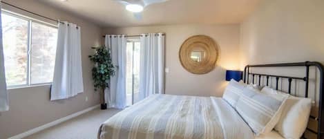 A bedroom with a bed, a ceiling fan, a window with curtains, and a plant.