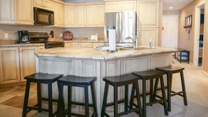 A kitchen with a large island, bar stools, a microwave, a refrigerator, and a sink.