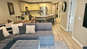 A modern living room with a grey sectional sofa, a small dining table, and a kitchen in the background.