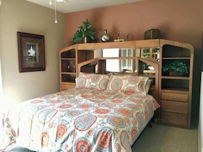 A bedroom with a bed, wooden headboard with shelves, a framed picture on the wall, and a potted plant. - Las Palmas Resort #1702 | All-Inclusive Amenities (Saint George)