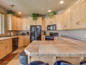 A kitchen with wooden cabinets, a central island, and a refrigerator. - Las Palmas Resort #1702 | All-Inclusive Amenities (Saint George)