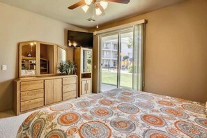 A bedroom with a bed, a dresser, a television, and a sliding glass door to a balcony. - Las Palmas Resort #1702 | All-Inclusive Amenities (Saint George)