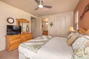 A bedroom with a bed, a television on a dresser, a ceiling fan, and a door leading to another room. - Las Palmas Resort #1904 | All-Inclusive Amenities (Saint George)