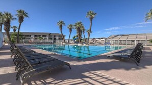 Una piscina con sillones de descanso, palmeras y un edificio al fondo.