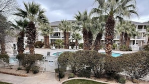Zona residencial con piscina rodeada de palmeras y un edificio de varios pisos al fondo.