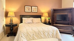 Un dormitorio con una cama grande, dos lámparas de noche, un televisor de pantalla plana y dos cuadros en la pared.