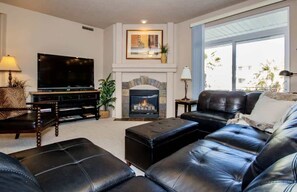 A living room with a fireplace, a television, leather sofas, and a large window.