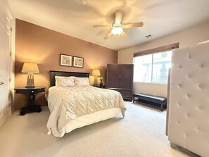 Une chambre à coucher avec un lit, des tables de chevet, un ventilateur de plafond et une fenêtre.