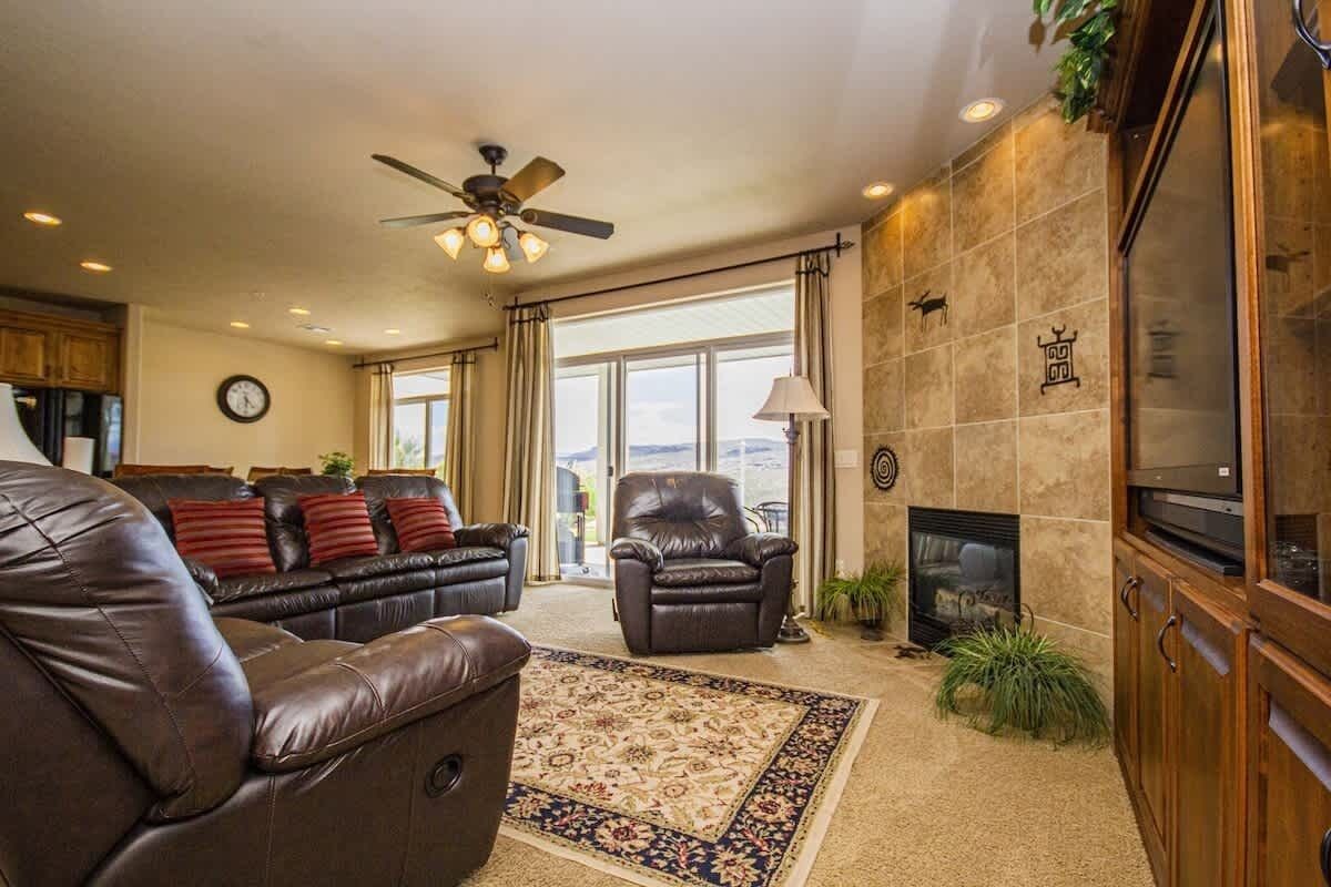 A living room with leather sofas, a fireplace, a ceiling fan, and a large window.