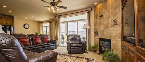 A living room with leather sofas, a fireplace, a ceiling fan, and a large window.