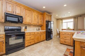 A kitchen with wooden cabinets, a black oven, a microwave, and a refrigerator.