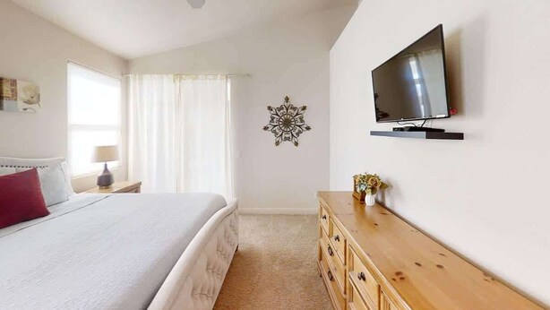 A bedroom with a bed, a TV mounted on the wall, a wooden dresser, and a decorative wall piece. - Las Palmas Resort #2018 | All-Inclusive Amenities (Saint George)