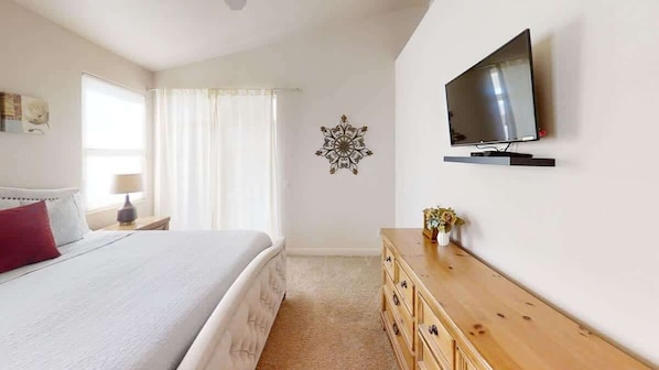 A bedroom with a bed, a TV mounted on the wall, a wooden dresser, and a decorative wall piece.