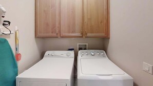 A laundry room with two washing machines, wooden cabinets above, and a red object on the wall. - Las Palmas Resort #2018 | All-Inclusive Amenities (Saint George)