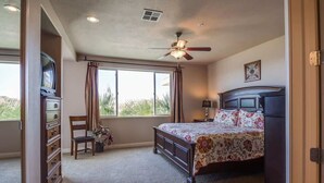 A bedroom with a bed, a dresser, a chair, a ceiling fan, and a window.