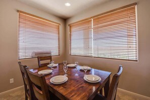 A dining room with a wooden table set for four, flanked by two windows with blinds. - Las Palmas Resort #2107 | All-Inclusive Amenities (Saint George)