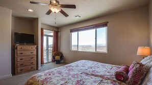 A bedroom with a bed, a ceiling fan, a television, and a window with a view.