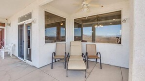 A covered patio area with a ceiling fan, two chairs, and a sliding glass door.