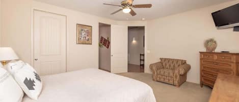 A bedroom with a bed, a ceiling fan, a dresser, a television, and a door leading to another room.
