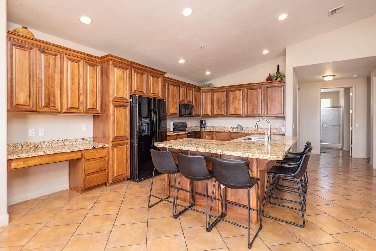 A kitchen with wooden cabinets, a granite countertop, a refrigerator, and bar stools.