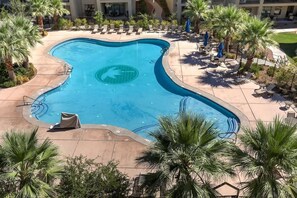 A swimming pool with a unique shape, surrounded by lounge chairs and palm trees.