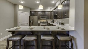 A modern kitchen with dark cabinets, a white countertop, and three bar stools.