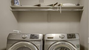 A laundry room with two front-loading washing machines and a shelf above them.