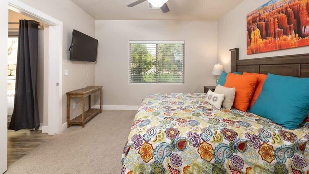 A bedroom with a bed, a ceiling fan, a window, and a painting on the wall.
