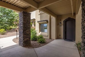 Une entrée de maison avec un pilier en pierre, une porte sombre et une fenêtre avec des stores.