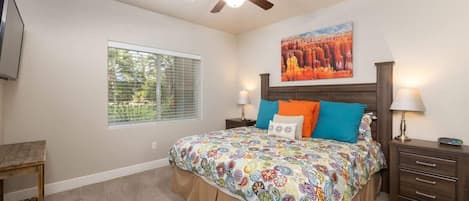 Un dormitorio con cama, ventilador de techo, ventana y un cuadro en la pared.