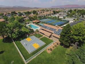 Vista aérea de una zona residencial con casas, piscina, canchas de tenis y paneles solares.
