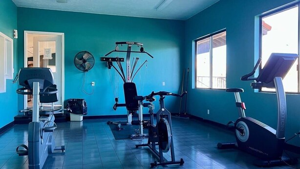 A gym with various exercise equipment, a large window, and a teal wall. - Sports Village Resort #H9 | All Amenities Included (Saint George)