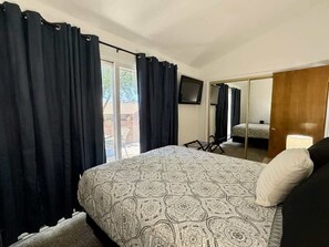 A bedroom with a bed, a chair, a TV, and a door leading to another room.