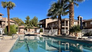 A swimming pool with clear blue water, surrounded by palm trees and a building with balconies.
