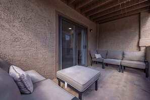 Ein überdachter Patio-Bereich mit einer Couch, einem Hocker und einer Schiebetür.