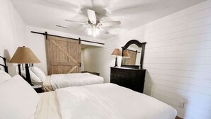 A hotel room with two beds, a ceiling fan, a wooden door, a dresser, and a mirror.