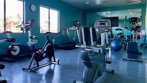 A gym with various exercise equipment, large windows, and a clock on the wall.
