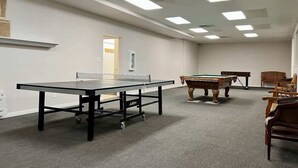 A room with a ping pong table, a pool table, and a billiards table.