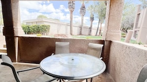 An outdoor patio with a round table and four chairs, a wooden ceiling, and a view of a garden and trees.