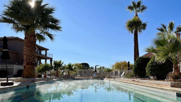 A clear swimming pool surrounded by palm trees and a building with balconies.