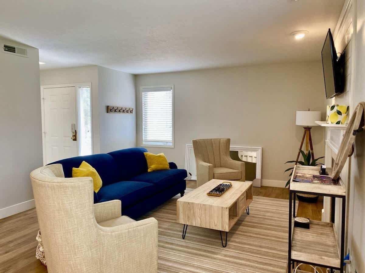 A living room with a blue sofa, beige armchairs, a coffee table, and a TV mounted on the wall.