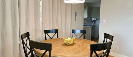 Een eetruimte met een ronde houten tafel, zes stoelen en een hangende lamp.